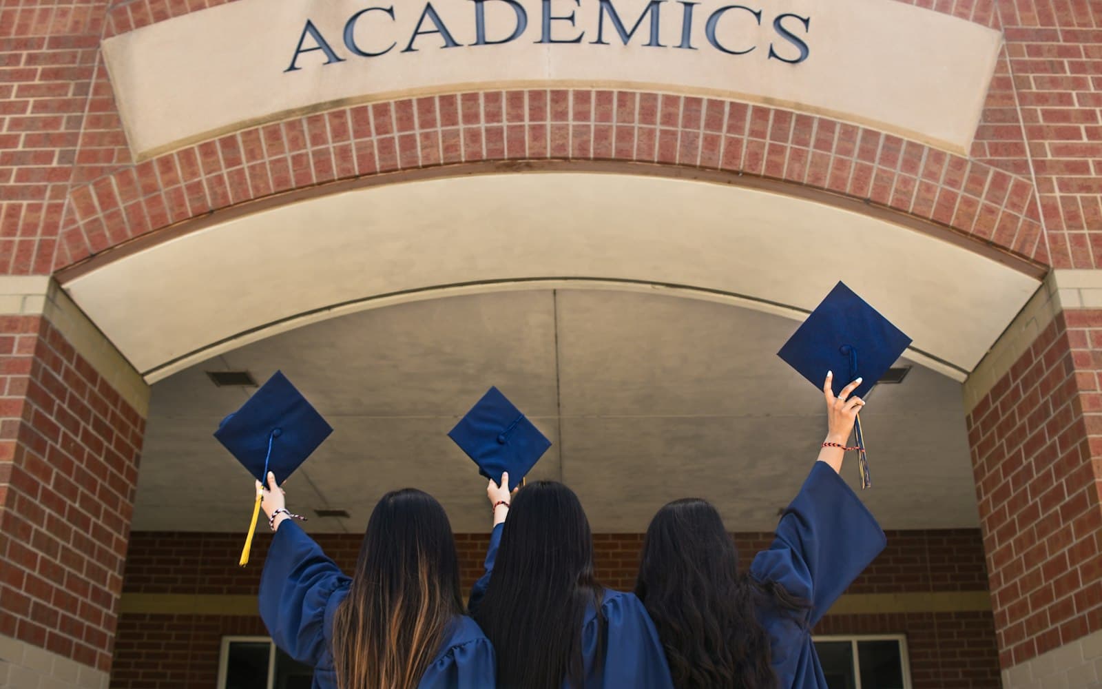 Three graduates in gowns tossing their caps in the air