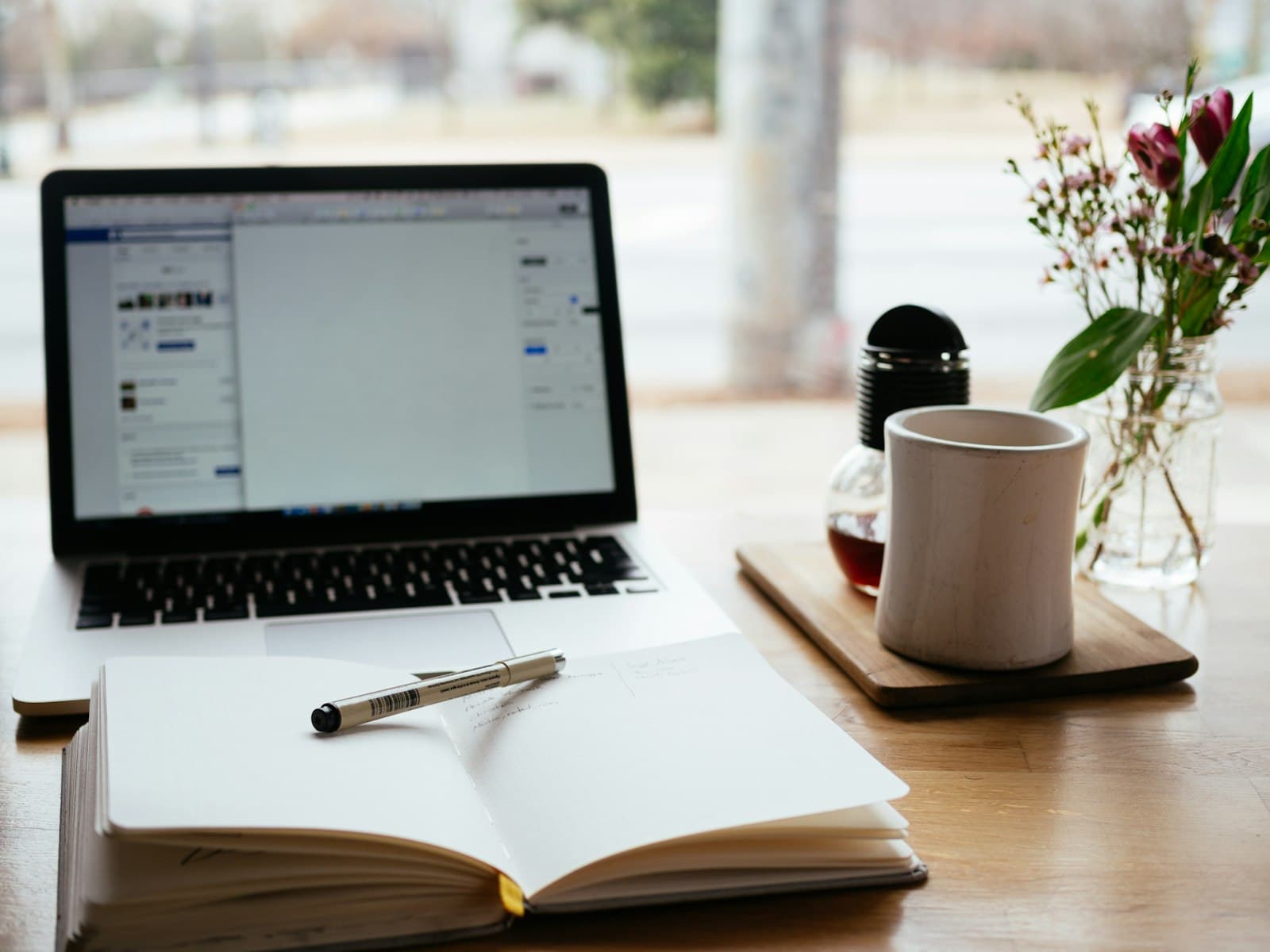 A laptop and an open notebook on a warm wooden desk