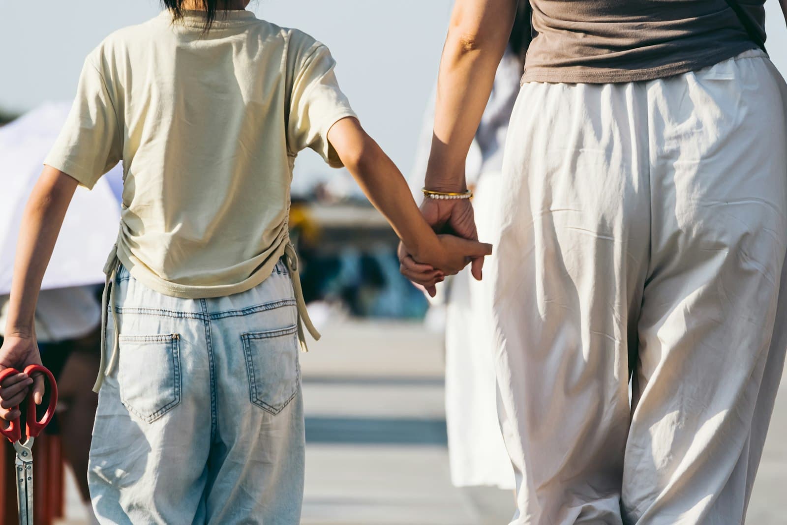 An adult and a child walking together, holding hands, seen from behind